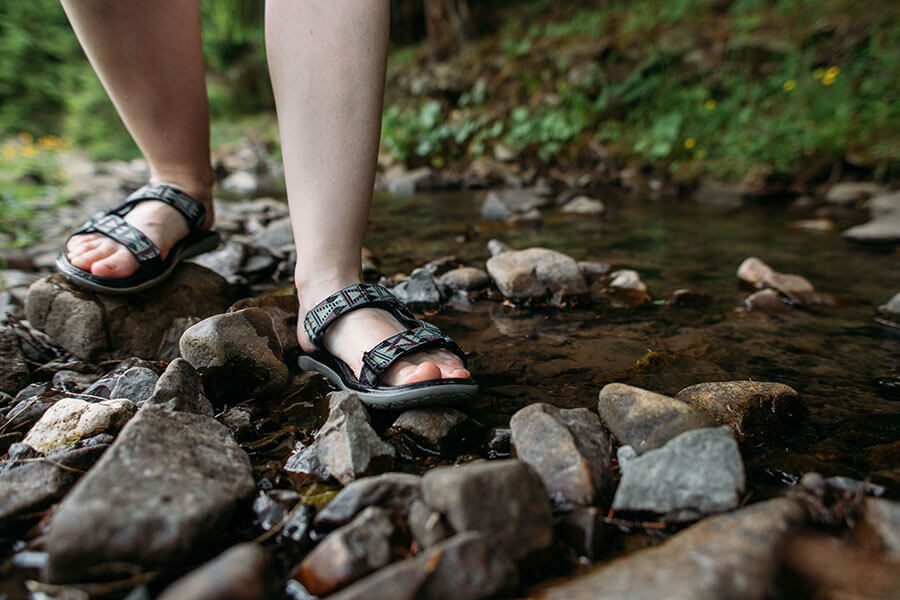 Frau mit Sandalen in einem steinigen Bachlauf