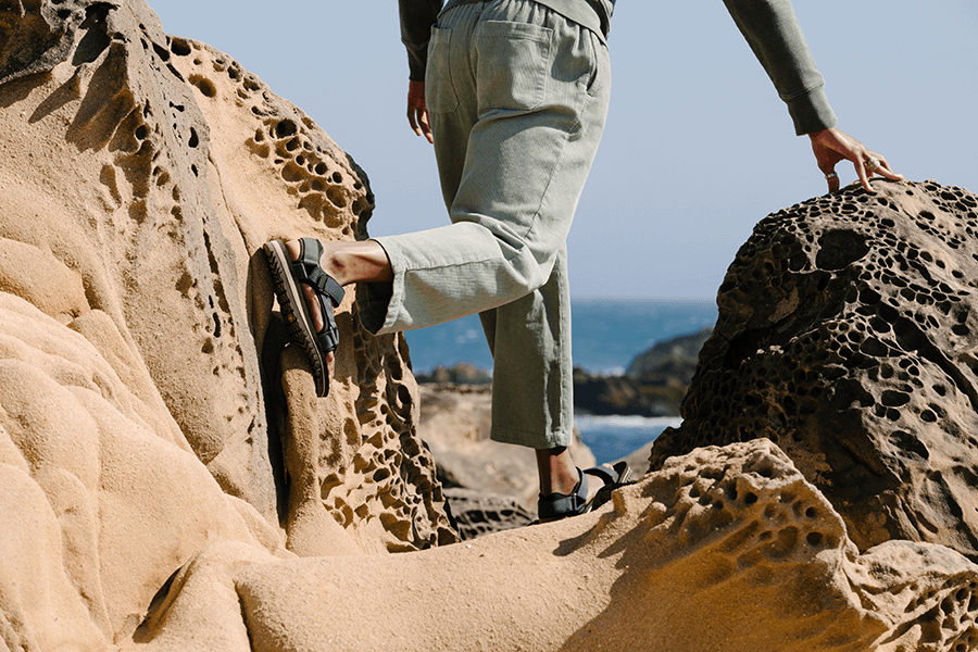 Mann mit Teva Sandalen am Strand im Sand zwischen Steinen