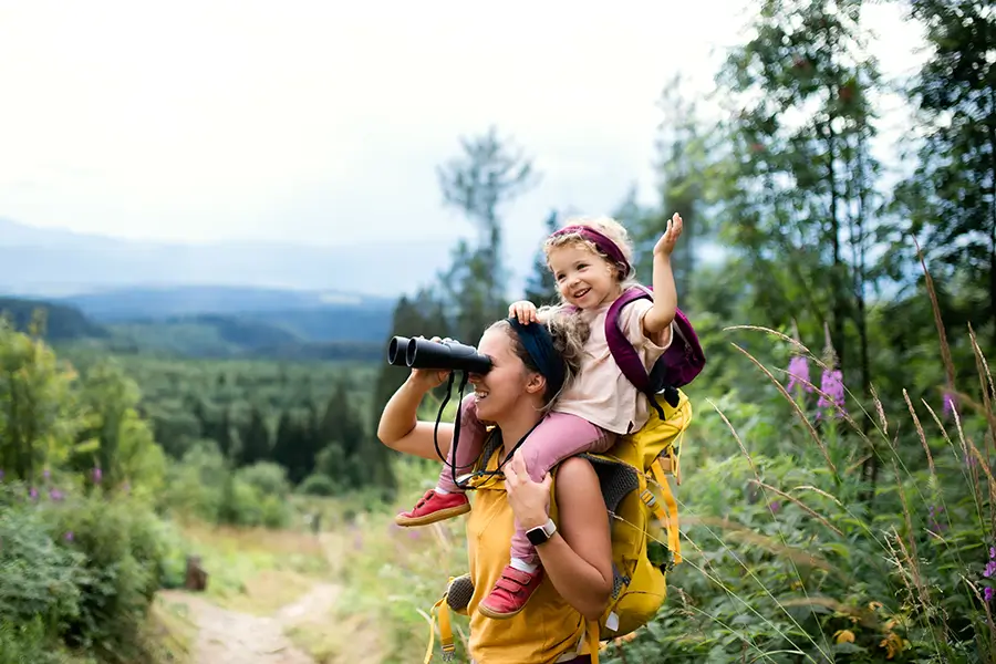 Mitter mit Kind auf den Schultern schaut durch ein Fernglas beim Wandern