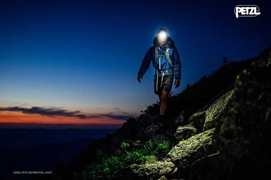 Person mit Stirnlampe nach Sonnenuntergang in den Bergen unterwegs  